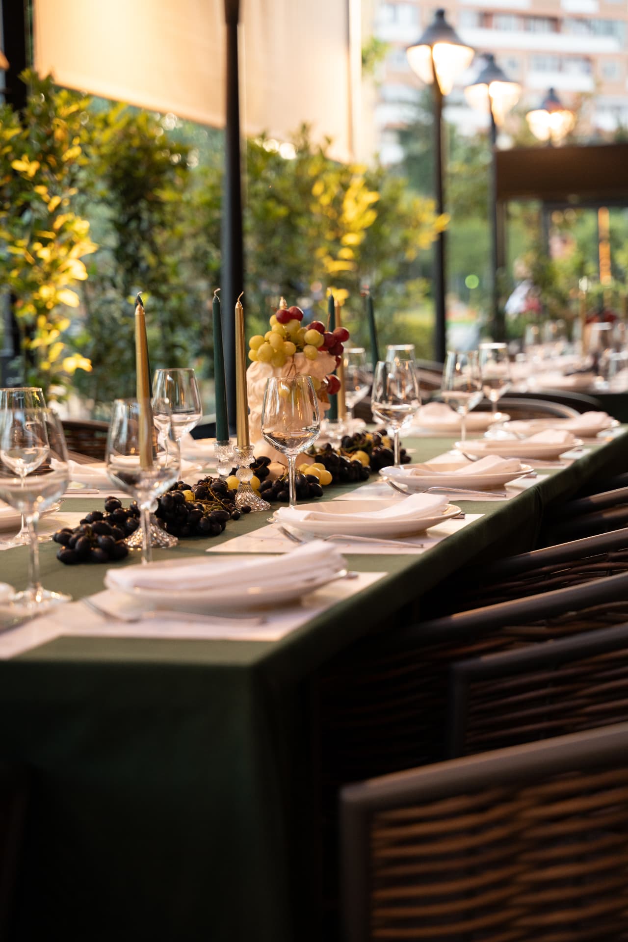 Long banquet table dressed in deep green with gold candles, set under the greenery of the ASADOR terrace
