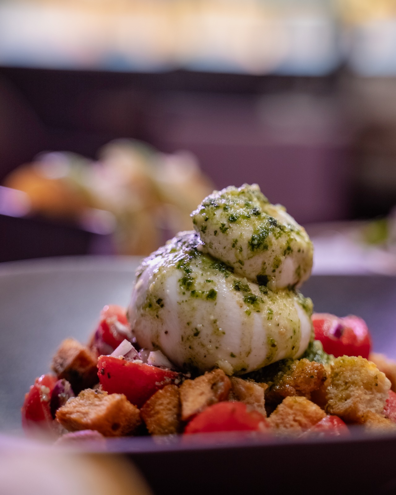 Burrata me pesto, domate qershi dhe krutona në pjatë të errët